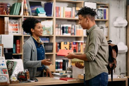 A young black female librarian helping a young black man in a library